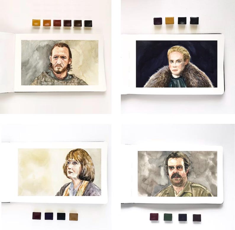 May include: A collection of four watercolor portraits in sketchbooks, each accompanied by small paint pans. The paintings depict individuals with distinct features, including a bearded person, a blonde person in fur, a person with glasses, and a mustachioed person.