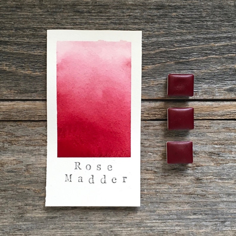 Op de afbeelding: Een aquarelverfstaal dat een verloop van roze naar rood laat zien. De verf is ge&euml;tiketteerd met "Rose Madder". Onder het staal zijn drie kleine vierkanten van dezelfde rode aquarelverf te zien.