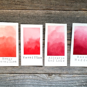 May include: Four watercolor paint swatches on white paper, labeled "Rouge Vermillion", "Vermillion", "Alizarin Red Lake", and "Rose Madder". The swatches show a gradient of red shades, from light to dark.