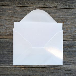 Puede incluir: Un sobre blanco con una solapa redondeada abierta que contiene una tarjeta rectangular blanca. El sobre tiene un acabado liso, mientras que la tarjeta presenta una superficie sutil y finamente texturizada. El dise&ntilde;o es limpio y neutro.
