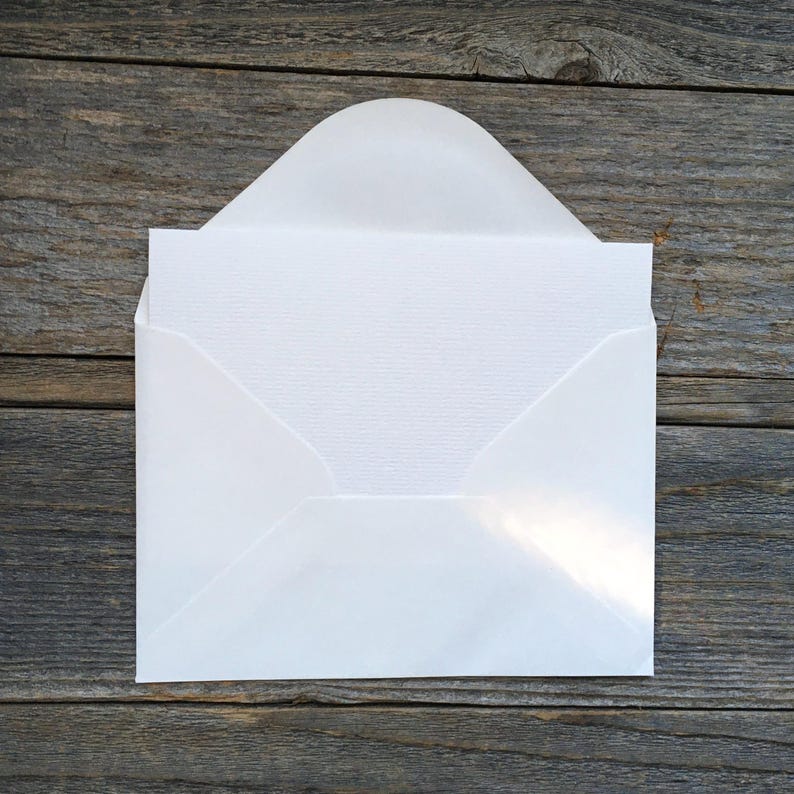 Puede incluir: Un sobre blanco con una solapa redondeada abierta que contiene una tarjeta rectangular blanca. El sobre tiene un acabado liso, mientras que la tarjeta presenta una superficie sutil y finamente texturizada. El dise&ntilde;o es limpio y neutro.