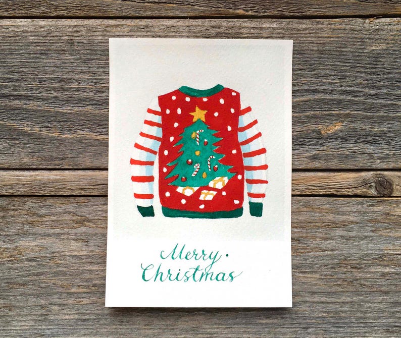 Puede incluir: Una tarjeta de felicitaci&oacute;n rectangular con una ilustraci&oacute;n en acuarela de un su&eacute;ter rojo con lunares blancos, mangas verdes con rayas rojas y un &aacute;rbol de Navidad verde central con una estrella amarilla, bastones de caramelo y regalos, con el texto Merry Christmas.