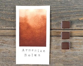 Könnte beinhalten: Eine rechteckige weiße Karte mit einem Aquarellfarbmuster, das von einem hellen Pfirsichton zu einem tiefen Rotbraun verläuft, mit dem Text "Armenian Bolus" darunter. Drei kleine, quadratische, dunkelbraune Aquarellnäpfchen liegen rechts daneben.