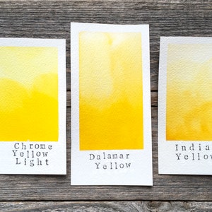 May include: Three rectangular watercolor swatches on white paper. The left swatch is labeled Chrome Yellow Light, the center is labeled Dalamar Yellow, and the right is labeled Indian Yellow. Each swatch displays a gradient of yellow pigment.