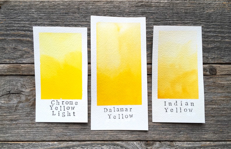May include: Three rectangular watercolor swatches on white paper. The left swatch is labeled Chrome Yellow Light, the center is labeled Dalamar Yellow, and the right is labeled Indian Yellow. Each swatch displays a gradient of yellow pigment.