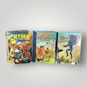 May include: Three vintage comic books with colorful illustrations. Titles include "Red Ryder and Gun-Smoke Gold", "Tarzan City of Gold", and "Zorro". The covers feature cowboys, Tarzan, and Zorro in action.