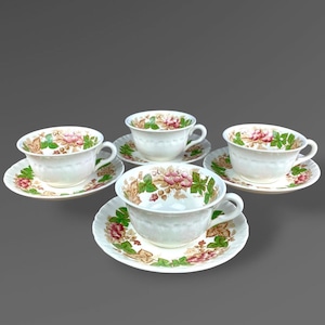May include: A set of four white ceramic teacups and matching saucers, each featuring a decorative rim pattern of green leaves, brown stems, and pink flowers. The cups have a rounded shape with a single handle and a smooth, glossy finish.