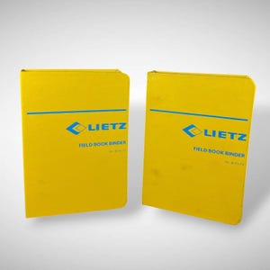 May include: Two yellow Lietz Field Book Binders. Each binder has a blue horizontal line across the top and the Lietz logo with the words "FIELD BOOK BINDER" printed in blue. The binders are rectangular and have rounded corners.