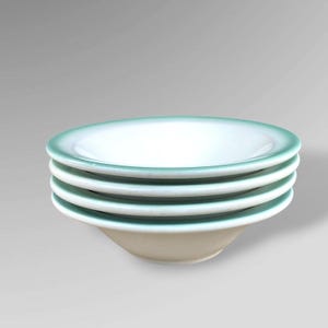 May include: A stack of four white ceramic bowls with a light teal rim. The bowls have a simple, classic design and are stacked neatly on top of each other. The bowls are suitable for serving soups, salads, or other dishes.