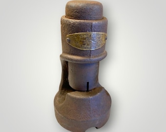May include: A vintage cable cutter made of weathered metal. The tool has a cylindrical body with a flared base and a top cap. A brass plate with text is affixed to the body. The cutter is a rusty brown color.
