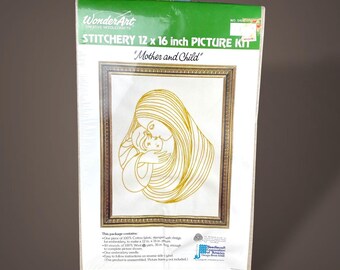 May include: A WonderArt stitchery 12 x 16 inch picture kit titled Mother and Child. The packaging features a green header and a central illustration of a gold line-art drawing of a parent and child inside a gold frame on a white background.