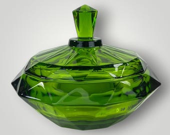 May include: A vibrant emerald green glass candy dish with a faceted, diamond-like geometric pattern. The bowl features a matching removable lid topped with a pointed, multi-faceted finial, creating a structured and reflective appearance.