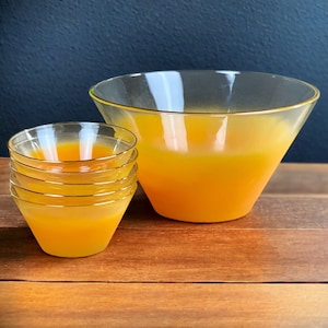 May include: A set of five clear glass bowls with gold rims. The bowls are stacked on top of each other, with the largest bowl at the bottom. The bowls are filled with a bright orange liquid.