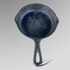 May include: A vintage cast iron skillet with a black handle and a number "3" on the side. The skillet is well-worn and has a dark patina.