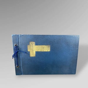 May include: A blue photo album with a gold-colored emblem that reads "Photographs." The album is bound with a blue string and has a textured cover. The album is rectangular and appears to be vintage.