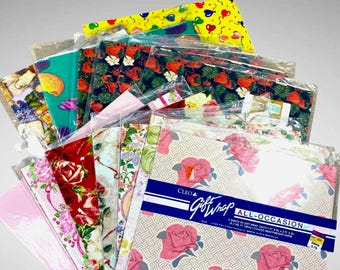 May include: A collection of folded gift wrap sheets in clear plastic sleeves. Patterns include pink roses on a beige geometric background, red roses, tropical leaves, and yellow balloons. The front package is labeled Cleo Gift Wrap All-Occasion.