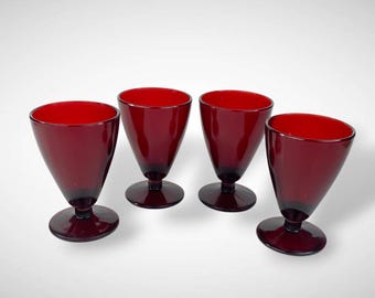 May include: Four ruby red stemmed glasses with a conical bowl and a circular base. The glasses are made of a dark red glass and are evenly spaced against a white background. The glasses are likely for serving beverages.