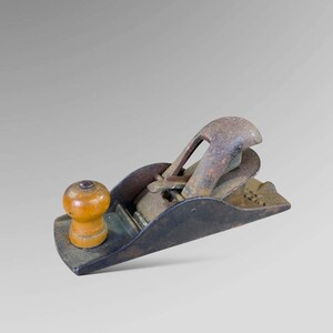May include: A vintage wooden and metal hand plane with a worn brown finish. The plane has a wooden handle and a metal blade.