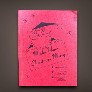 May include: A vintage Christmas booklet with a red cover featuring a Santa Claus illustration holding a sign that reads "Make Your Christmas Merry." The booklet includes text about Christmas tree decorations, aprons, and cookies.