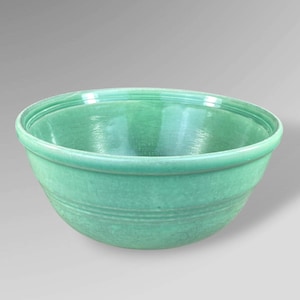 May include: A solid, light green ceramic mixing bowl. The bowl has a rounded shape with a wide rim and a series of horizontal ridges around the lower portion. The interior is smooth and glossy, while the exterior has a matte finish.
