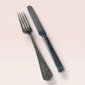 May include: An antique silver fork and knife set. The fork has four tines and a decorative handle. The knife has a rounded blade and a matching handle. Both pieces show signs of age and wear, with a slightly tarnished appearance.