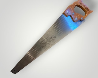 May include: A vintage hand saw with a wooden handle and a silver blade. The handle is a light brown color with a decorative design. The blade has the text "Gamble" and "A-M-E-R-I-C-A-N" printed on it.