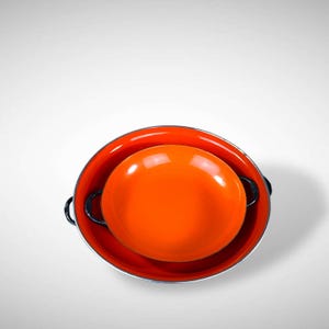 May include: Two orange enamel pots with black handles. The smaller pot is nested inside the larger pot.
