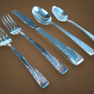 May include: Five pieces of silverware, including a fork, knife, and three spoons, all with an ornate design. The silverware is made of polished silver and has a reflective surface.