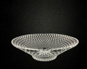 May include: A clear glass bowl with a wide, shallow design. The bowl features a textured pattern of small, raised dots across its surface. The bowl is set against a black background, highlighting its transparent quality and intricate texture.