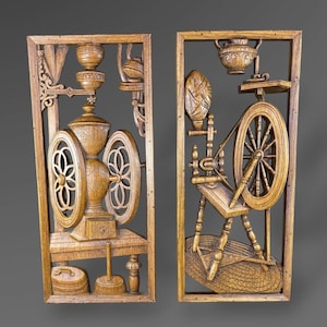 May include: Two wooden wall panels with carved relief designs. One panel features a coffee grinder, the other a spinning wheel. Both are framed in a light brown wood, showcasing detailed craftsmanship and a rustic aesthetic.