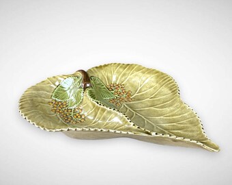 May include: A decorative, leaf-shaped ceramic serving dish. The dish is light green with detailed leaf veining and a textured edge. It features clusters of small, orange-yellow berries and green leaves. The dish is approximately 12 inches long.