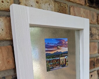 May include: A white framed magnetic board with two photos attached. The top photo shows a cityscape at sunset with mountains in the background. The bottom photo shows a rocky landscape with a cloudy sky.