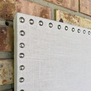 May include: A white fabric bulletin board with silver decorative tacks around the edge.