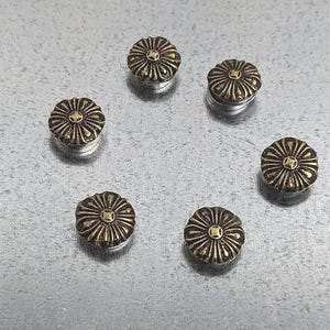 May include: Six gold-toned metal flower-shaped magnetic buttons with a silver backing.