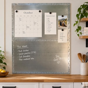 May include: A rectangular galvanized steel magnetic wall board with a riveted border. The upper section holds a paper October calendar, a grocery list, a photo, and a note. The lower section features handwritten text: This Week, tasks, and You Got This.