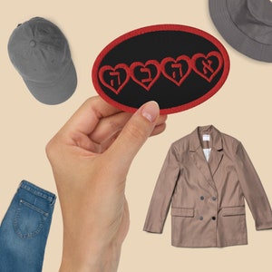 May include: A red embroidered patch with three hearts and Hebrew text on a black background. The patch is being held by a hand.