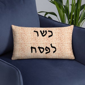 May include: Rectangular decorative cushion with a matzah-like pattern. The cushion features the Hebrew text "Kosher for Passover" in black. The cushion is resting on a blue chair.