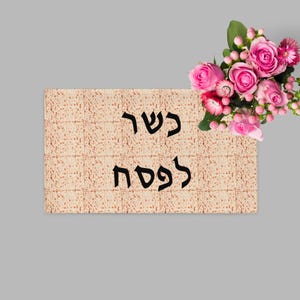 May include: A matzah, a traditional unleavened bread, with the Hebrew text "Kosher for Passover" in black. A bouquet of pink roses and buds is in the upper right corner, against a grey background.