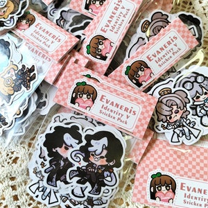 Puede incluir: Un conjunto de pegatinas con personajes del juego Identity V. Las pegatinas están en una variedad de poses y expresiones, y están impresas en papel transparente y brillante. Las pegatinas están empaquetadas en una bolsa de plástico transparente con un fondo a cuadros rosa y blanco. El texto en la bolsa dice "Evaneris Identity V Sticker Pack".