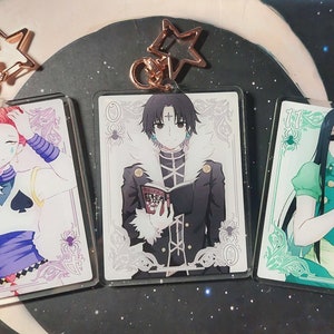 May include: Three anime character keychains featuring a pink and white character with a spade symbol, a black and white character holding a book, and a green and white character with long black hair. Each keychain has a gold star charm.