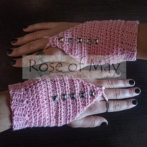 May include: Pink crocheted fingerless gloves with silver pyramid-shaped studs. The gloves have a pointed finger opening and a strap that wraps around the wrist.