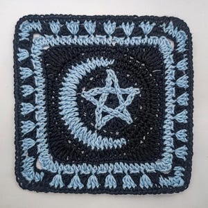 May include: A square, crocheted item featuring a five-pointed star in the center. The star and concentric circles are light blue against a black background. The border is also light blue with tassel-like details.