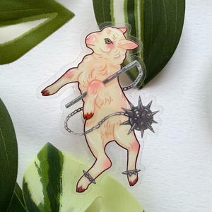 Könnte beinhalten: Ein durchsichtiger Aufkleber mit einem hell cremefarbenen Lamm, das auf seinen Hinterbeinen steht. Das Lamm hat eine rosa Schattierung an Ohren und Hufen und hält eine silberne Kette, die mit einem dunkelgrauen Stachelmorgenstern verbunden ist.