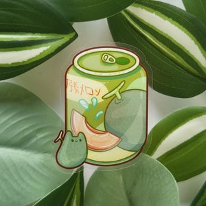 Könnte beinhalten: Ein Aufkleber mit einer grünen Dose, in der sich eine Melone befindet. Die Dose trägt den japanischen Text "Melon Soda". Links neben der Dose befindet sich ein kleines grünes Wesen.
