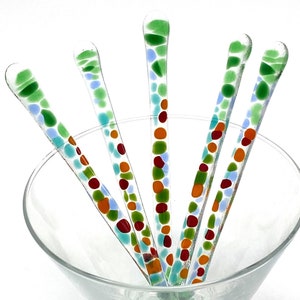 May include: Set of four glass stirring sticks with colorful dots in shades of red, orange, green, and blue. The sticks are in a clear glass martini glass.