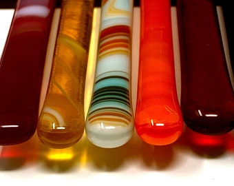 May include: Six glass rods, each with a different color and pattern. The rods are arranged horizontally, with the red rod on the left and the black rod on the right. The rods are all about the same length and thickness.