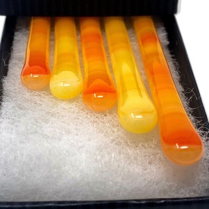 May include: Set of five glass stirring sticks in a black box. The sticks are ombre, transitioning from yellow to orange.