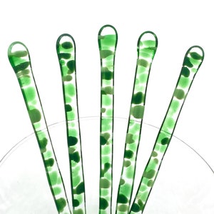 May include: Five green glass stirring sticks with white flecks. The sticks are in a clear glass bowl.