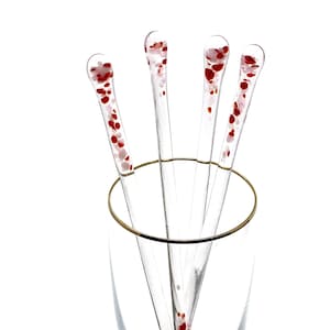 May include: Four clear glass stirring sticks with red and white flecks in a clear glass champagne flute.