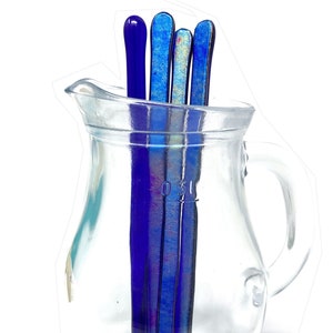 Puede incluir: Cuatro palitos de vidrio para remover en una jarra de vidrio transparente. Los palitos son azules e iridiscentes.